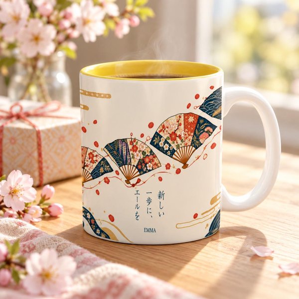 Personalized Japanese mug with a white handle and yellow inside beside spring blossoms and a gift: folding fan artwork with the phrase cheers to your new step and the sample name EMMA, a new beginning gift.