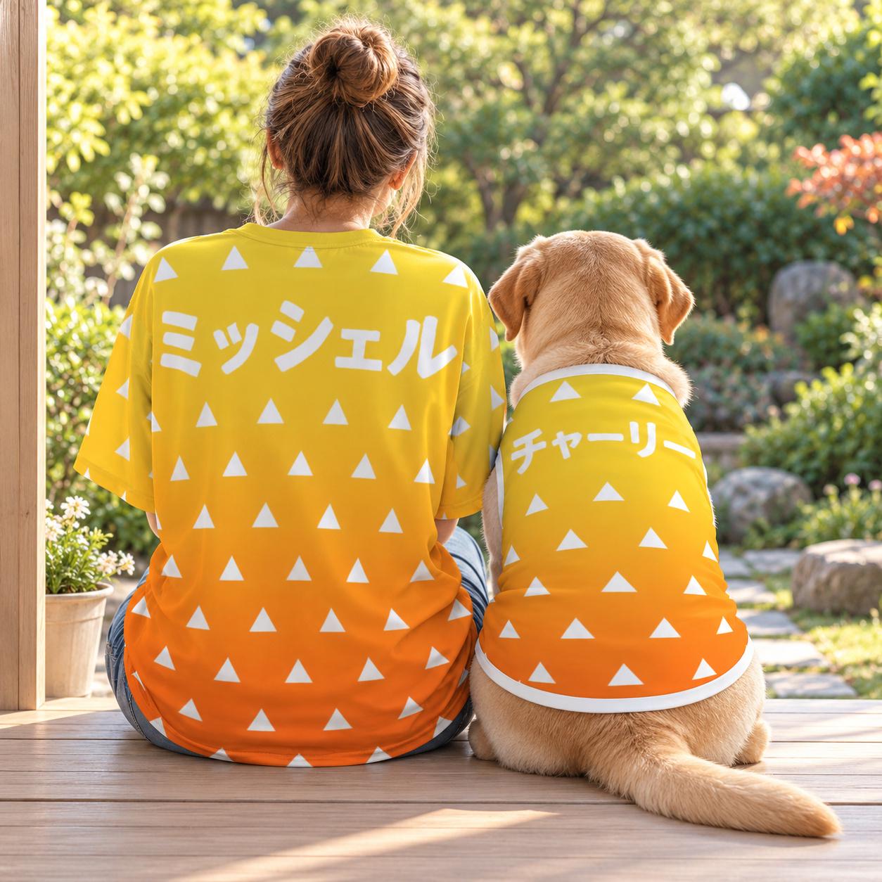 Matching dog and owner shirts seen from behind: a person and a Labrador sit side by side on a wooden porch in the yellow-to-orange sunrise triangle design, with the names Michelle and Charlie in Japanese katakana.